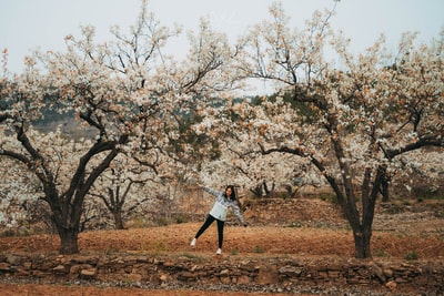 Wearing a white long sleeve shirt and blue denim jeans women stood on the brown field, was dressed in brown
